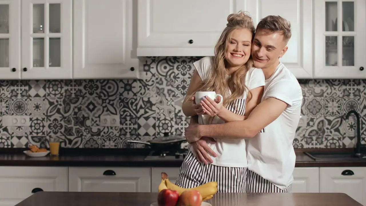 A couple standing close together in a bright kitchen during a calmer moment