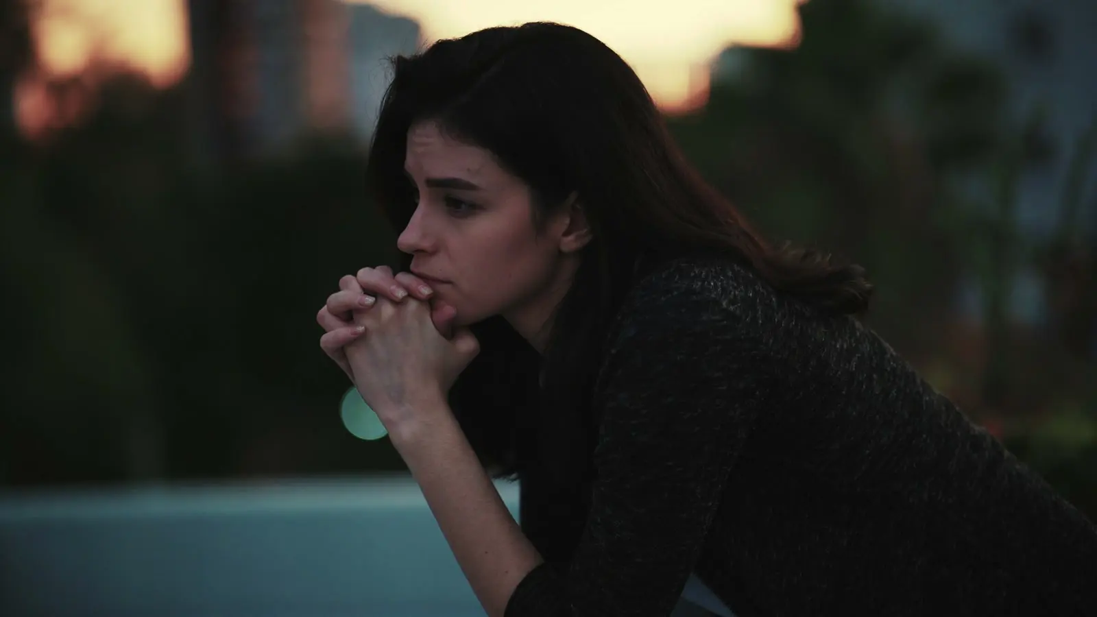 A woman sitting alone outdoors at dusk in a private reflective moment