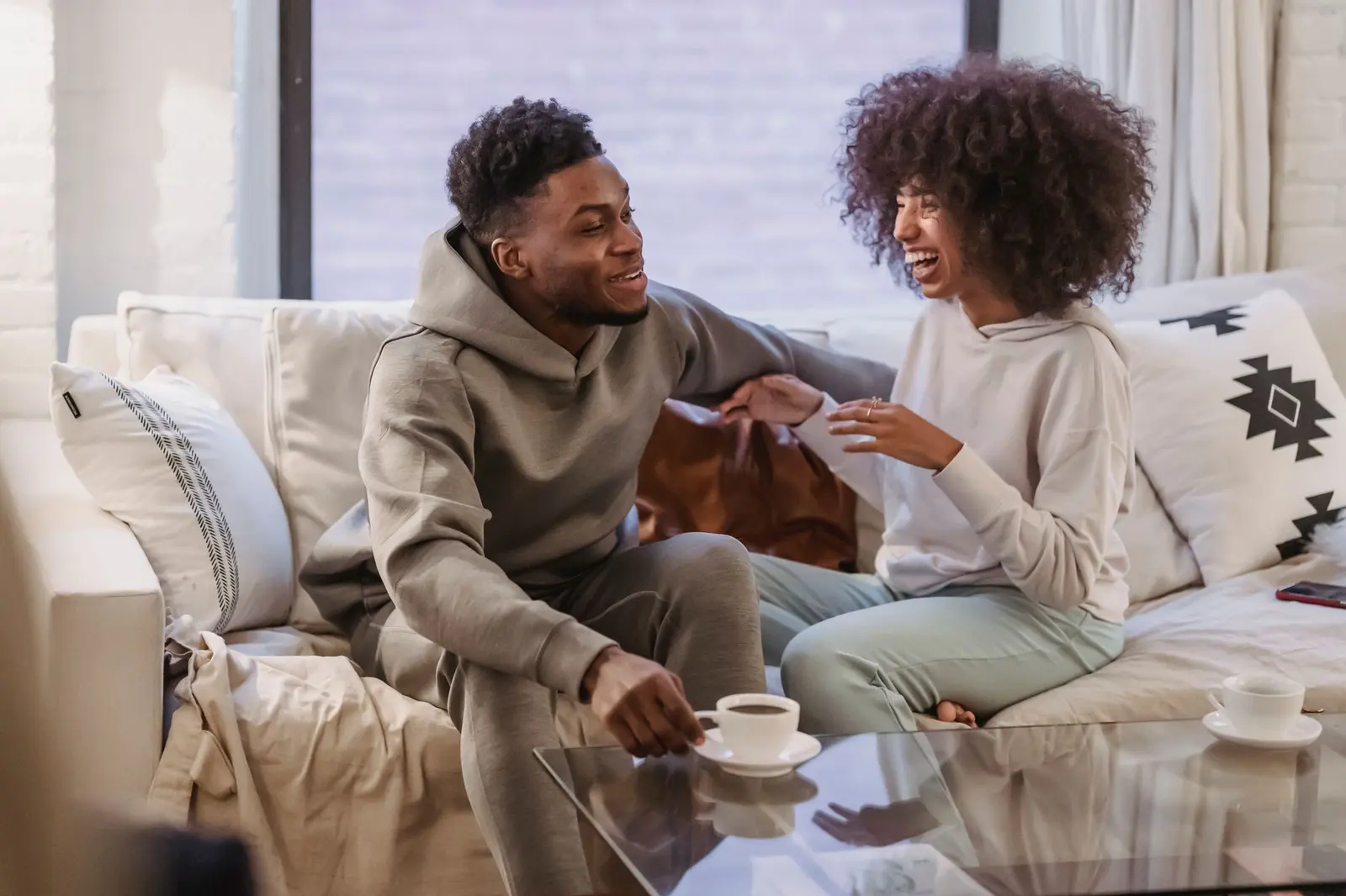 Two people smiling during a calm sofa conversation, showing a relationship pace that still feels warm and connected