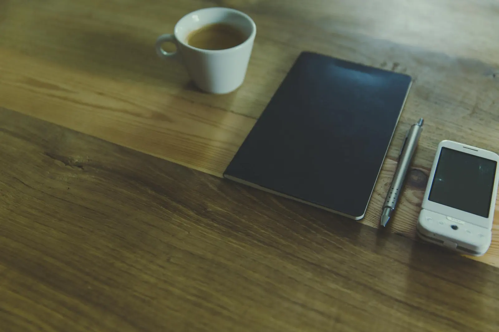 A quiet desk with coffee, notebook, pen, and a phone with a blank screen for private relationship reflection