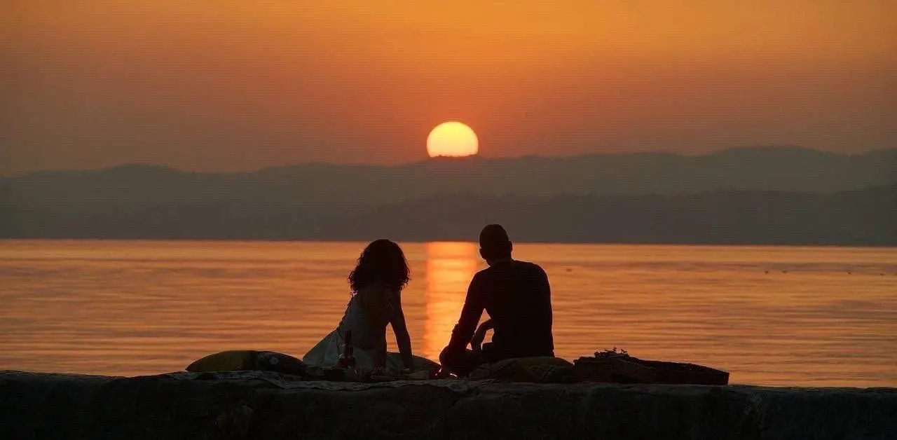 A couple sitting quietly near water at sunset while considering the next step