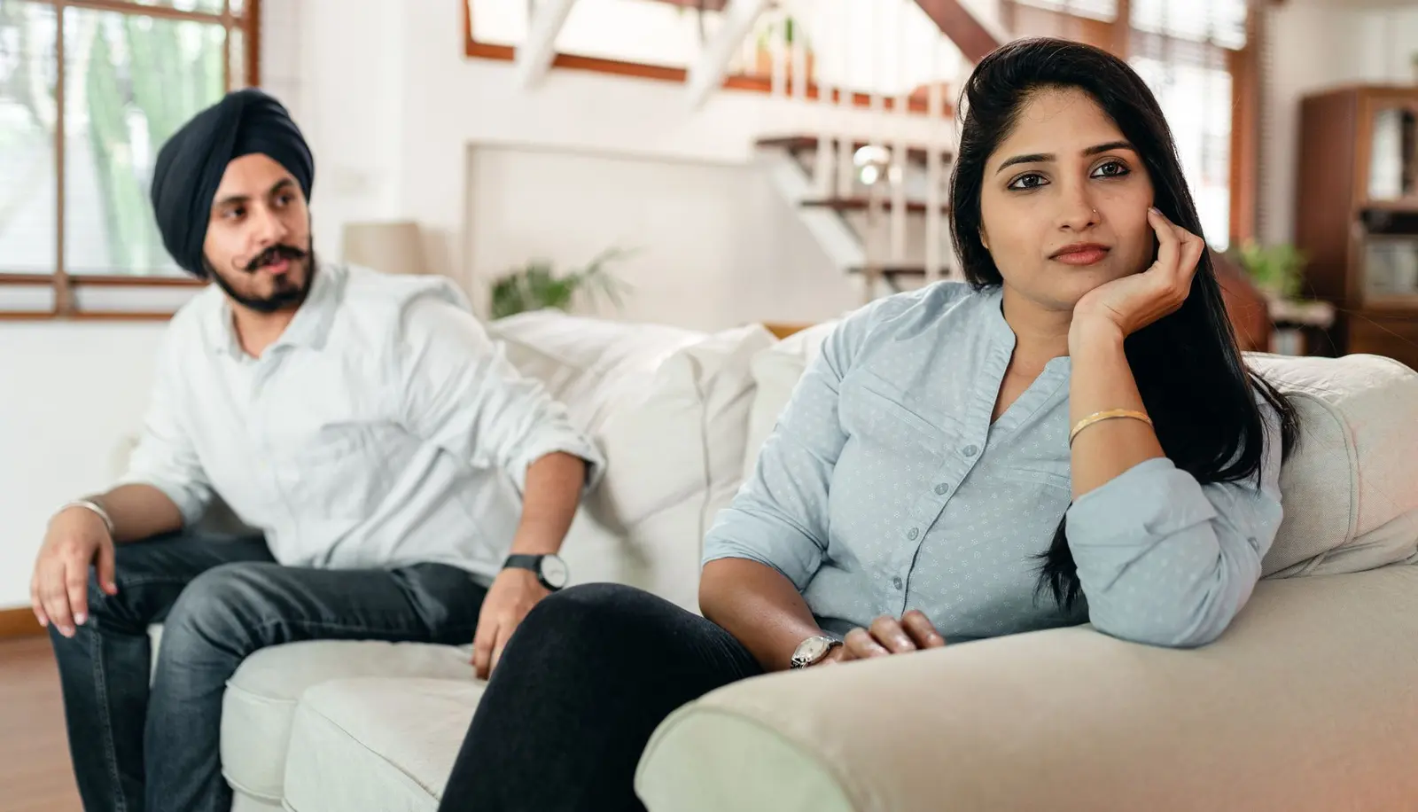 A couple sitting apart on a sofa with one partner turned away.