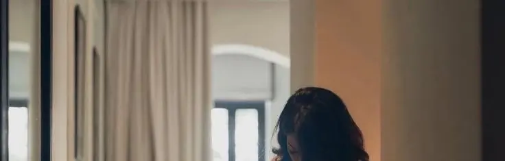 A person standing near a window in warm indoor light, reflecting before deciding what the message means.